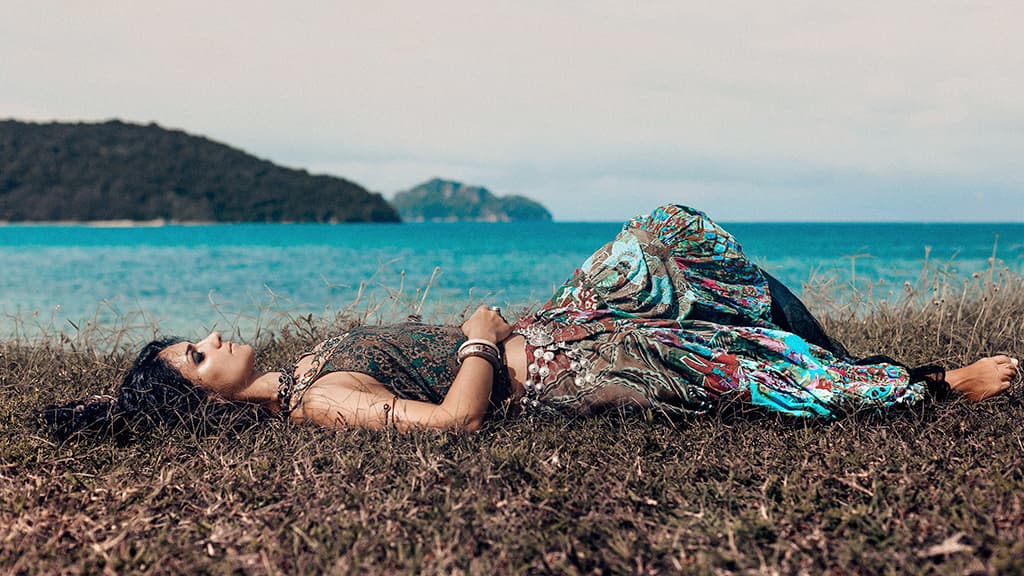 Mujer con atuendo bohemio tumbada junto al mar