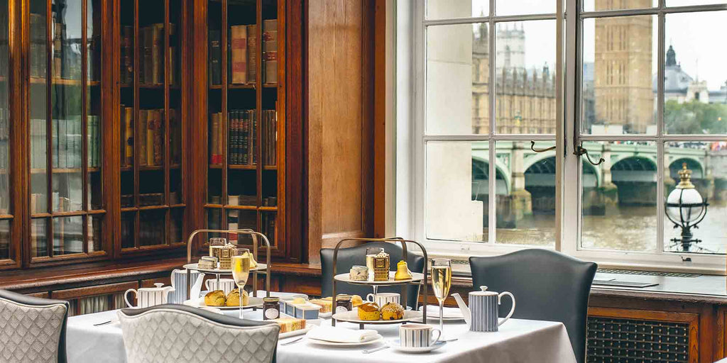 Afternoon tea set up on a table in a hotel near a large window looking out over the river Thames and Big Ben