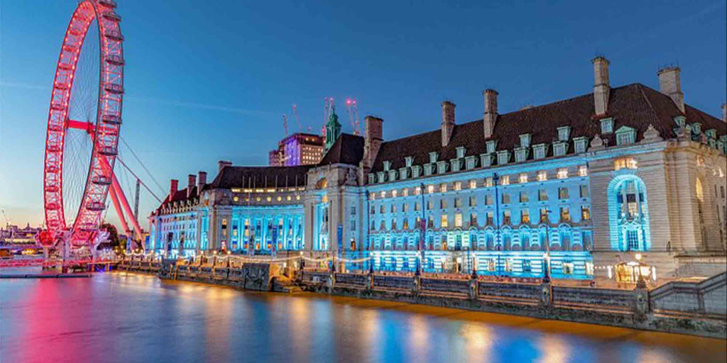 Evening time, overlooking the London Marriott Hotel, County Hall with lights reflecting off of the darkened water of the River Thames and red lights glowing around The London Eye