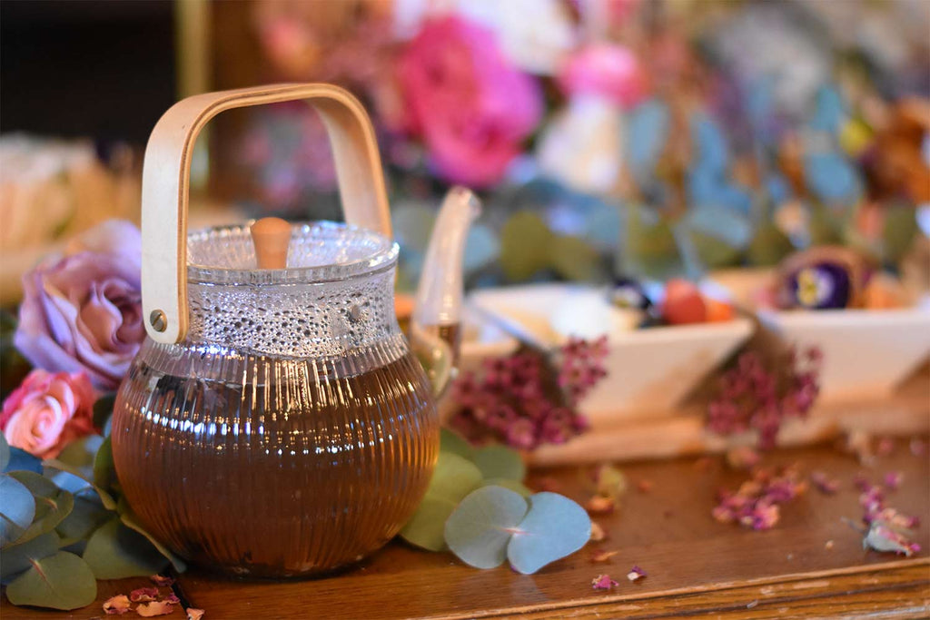 Glass teapot with oolong tea in a floral afternoon tea setting