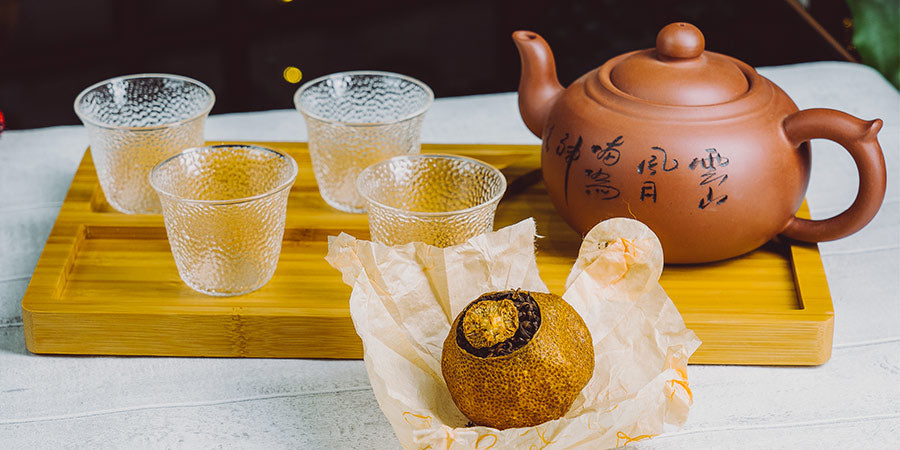 Pu erh tea in a dried tangerine with a traditional clay teapot and hammered class cups