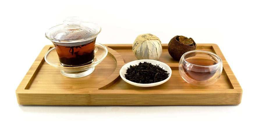 Glass cup filled with tea and mixed types of loose leaf ta on bamboo tray