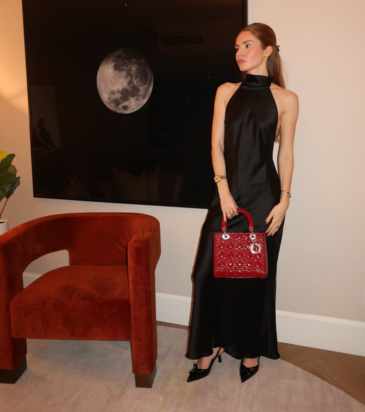 Fille dans une longue robe noire tenant un sac Lady Dior verni rouge dans une pièce avec une chaise rouge et une photographie de lune noire