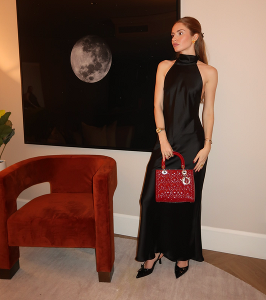 Girl in a long black dress holding a red patent lady dior bag in a room with a red chair and a black moon photograph