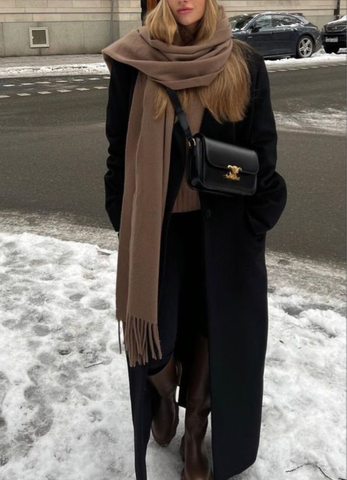 fille dans la rue enneigée avec un manteau noir, des bottes, une écharpe marron et un sac triomphe Céline noir