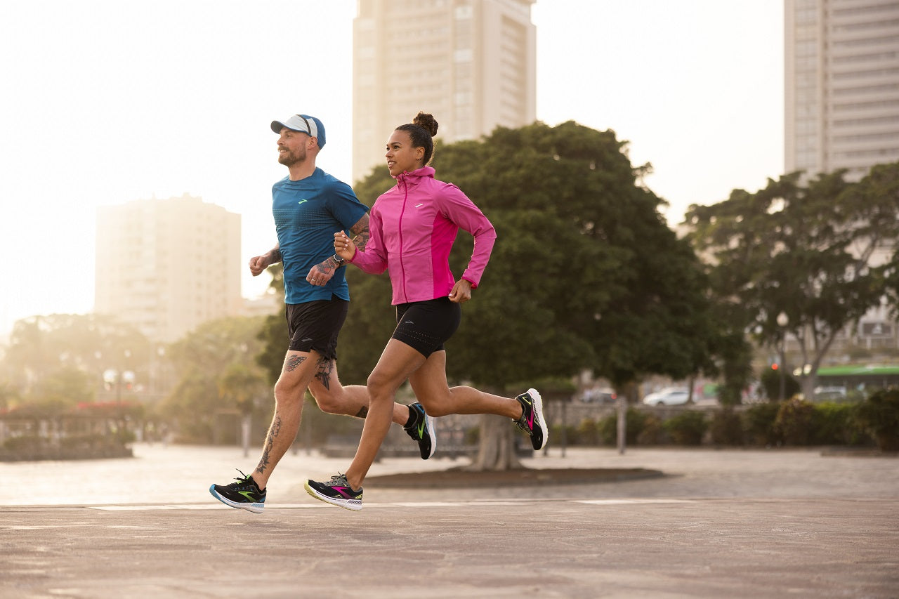 Male and female runner running side by side in sunny city environment