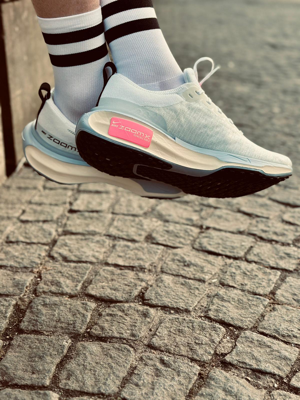 Side view of runner's feet in a pair of white Nike ZoomX Invincible 3 running against a cobbled street background