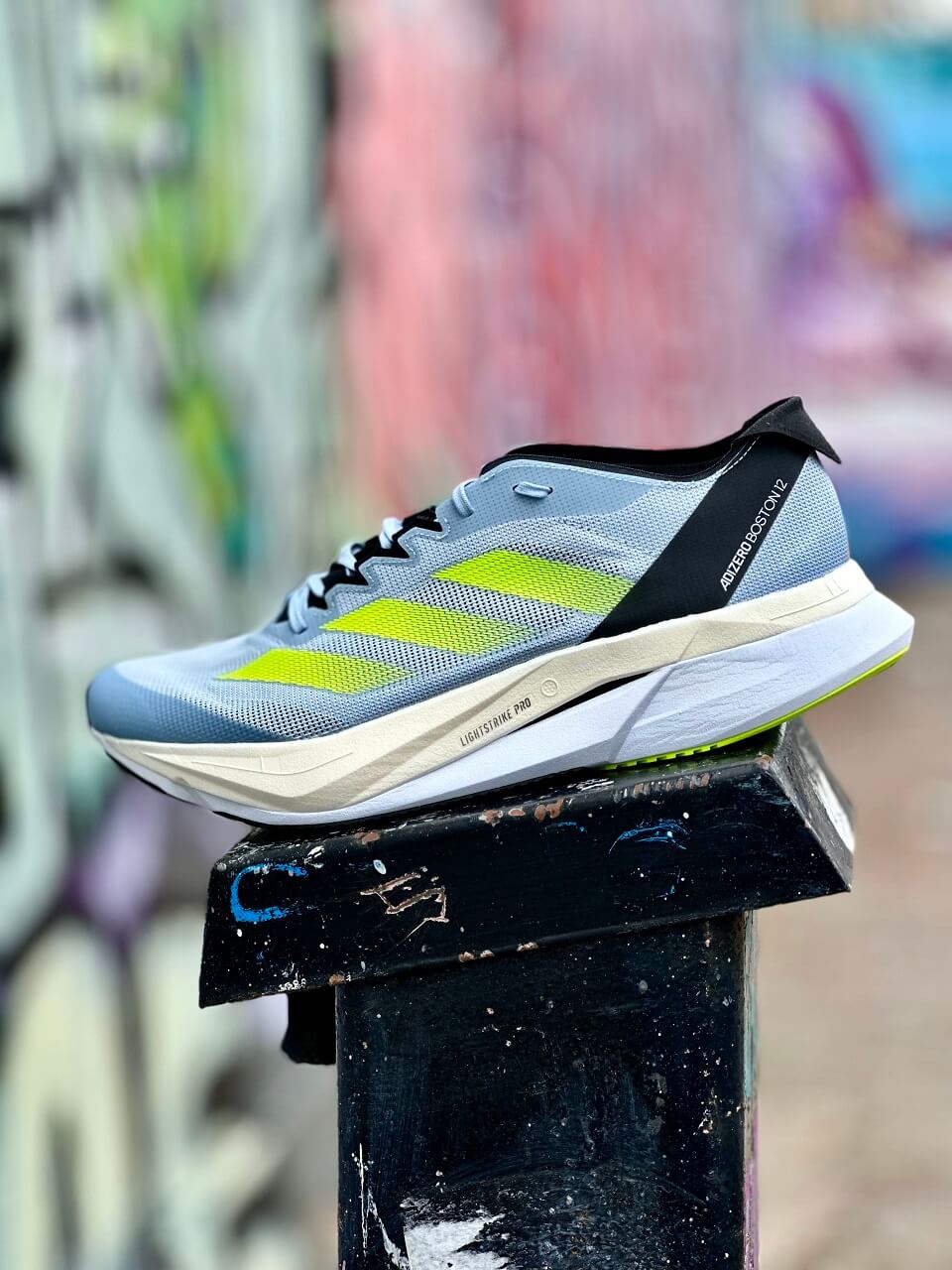 adidas running shoe propped on post in front of graffiti wall