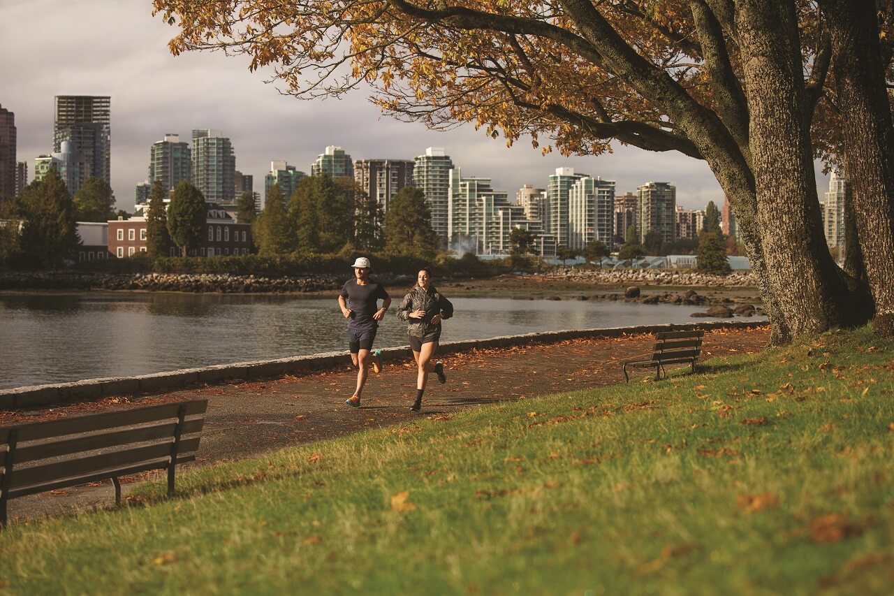 Two runners running side by side through a park with water in the city