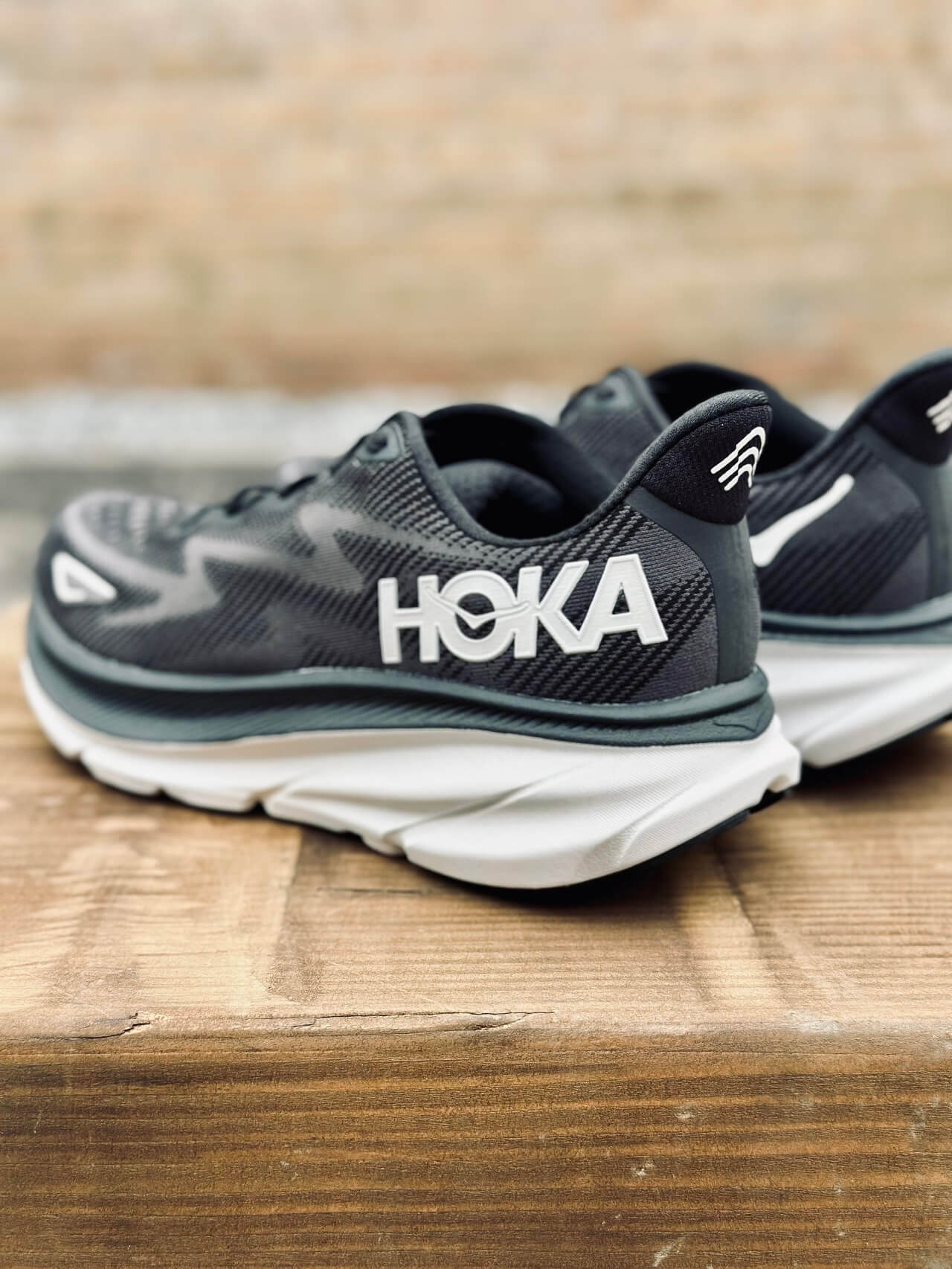 HOKA Clifton 9 running shoes in black on wooden bench
