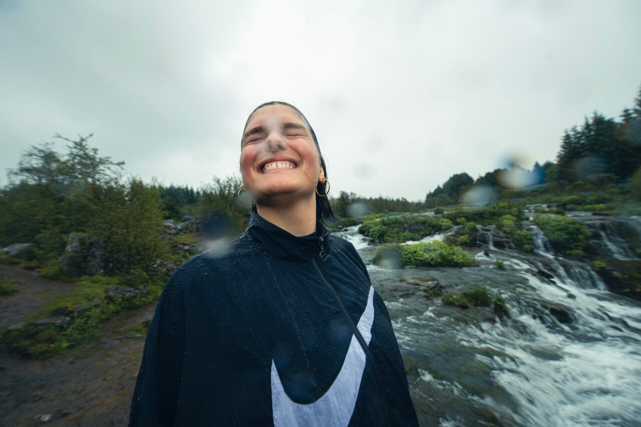 Female runner in Nike jacket smiling in the rain in front of a waterfall