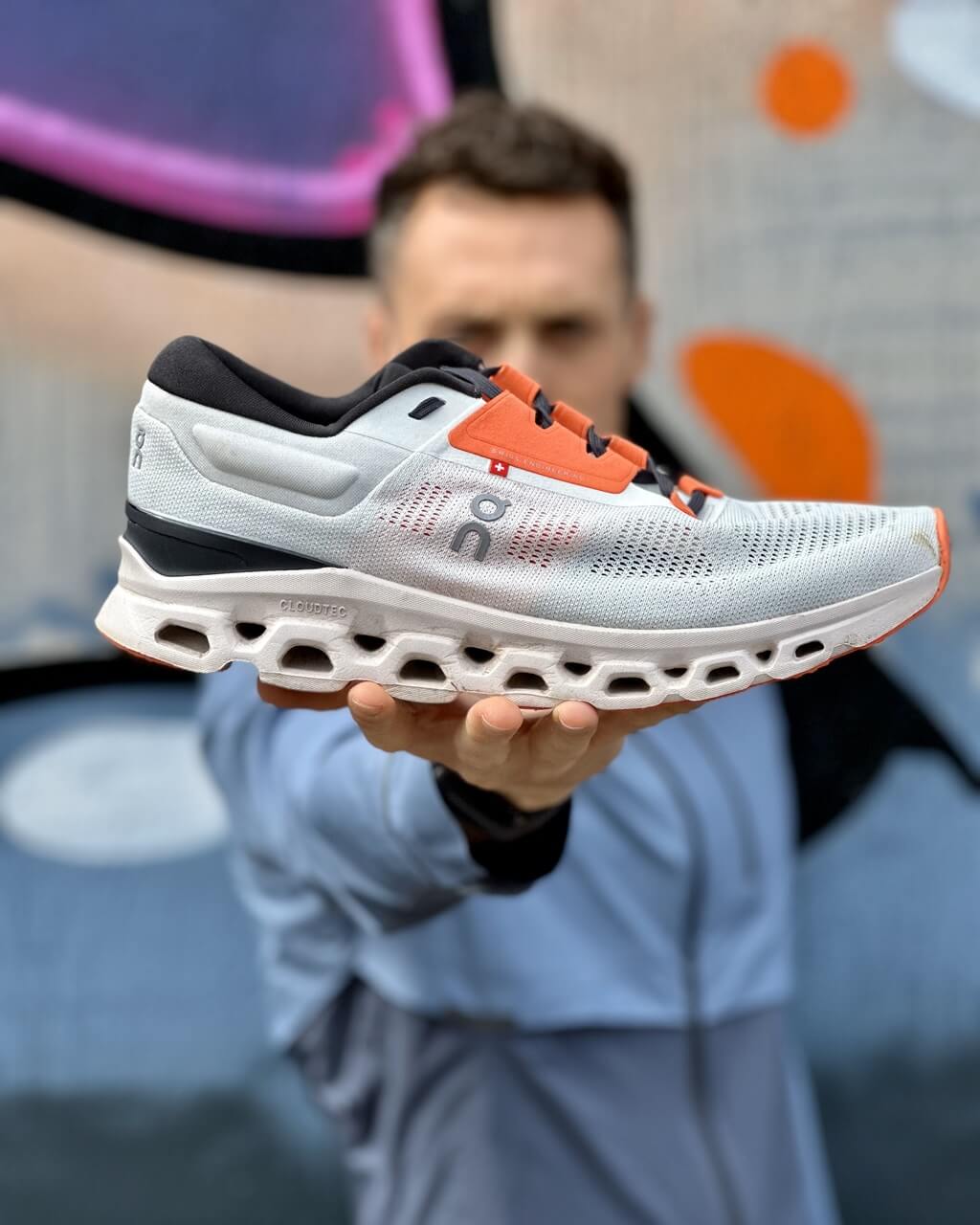 Man holding an On Cloudstratus 3 running shoe in front of graffiti wall