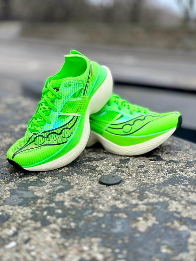 Pair of Saucony Endorphin Elite road racing shoes in slime green against concrete background