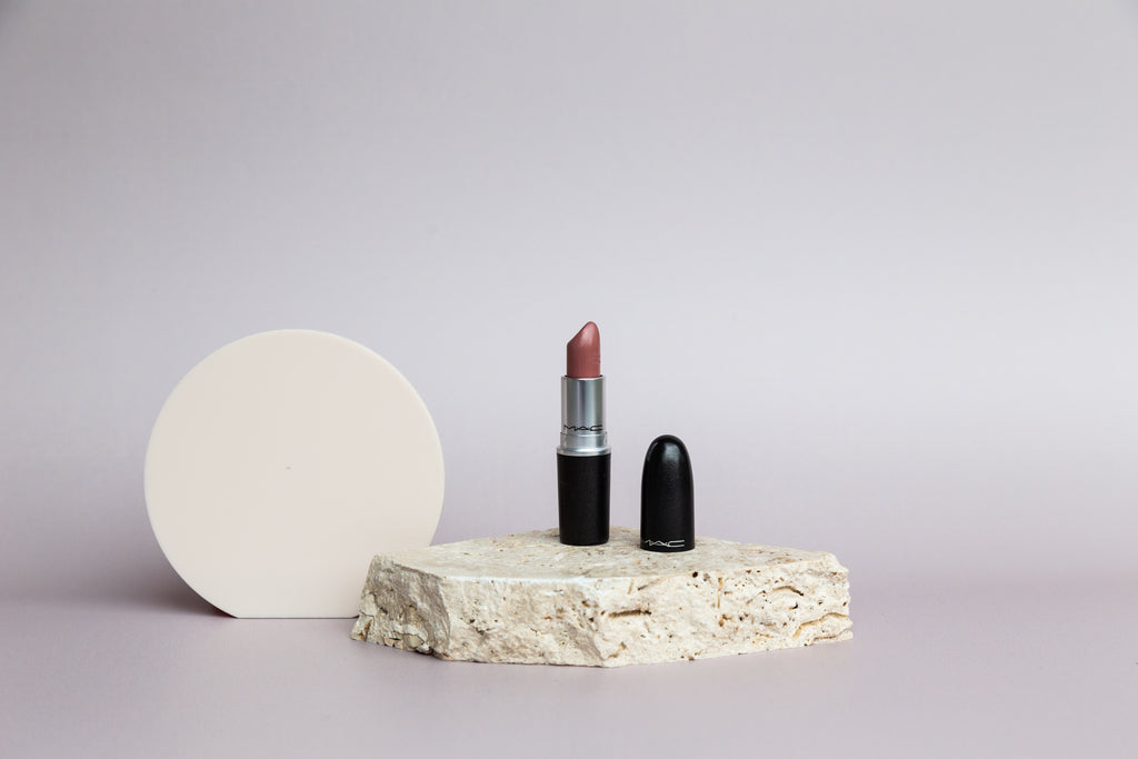 Open lipstick tube sitting on travertine block against grey backdrop