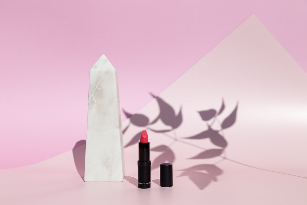 Pink lipstick next to a marble obelisk and pink backdrop