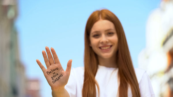 girl with encouraging message that says "believe in your dreams" written on her hand