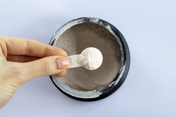 hand scooping dose of white electrolyte powder out of a black jar
