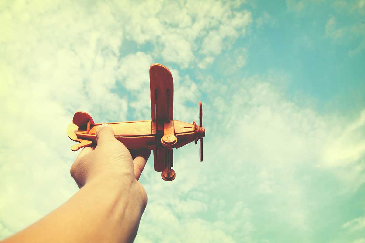 A hand holding a toy plane in the sky