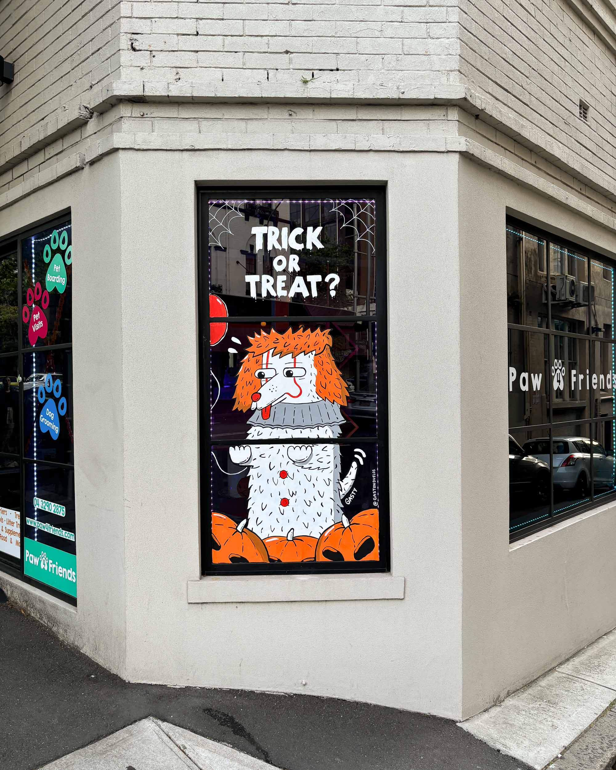 Festive window painting at a pet shop in Darlinghurst, Sydney, adorned with cute dogs in Halloween costumes, creating a delightful atmosphere.