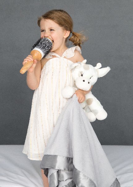 Toddler singing into hairbrush holding stuffed animal and baby blanket