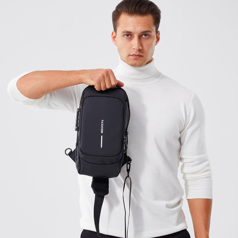 Man in a white turtleneck holding a compact black travel sling bag with visible brand logo, demonstrating the bag's portable design and ease of carrying for modern, on-the-go lifestyle.