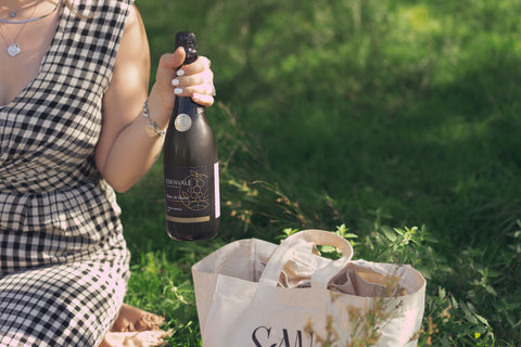 Sarah holds a bottle of alcohol-removed Edenvale Blanc de Blanc on a picnic blanket with a Sansorium bag at her feet.