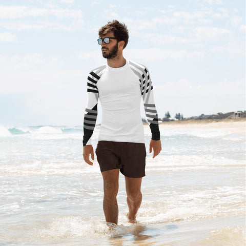 Young man walking in the beach shore line wearing a white long sleeve men's rash guard with grey and black patterns on its sleeves.