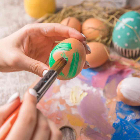 Image shows a hand painting an Easter egg