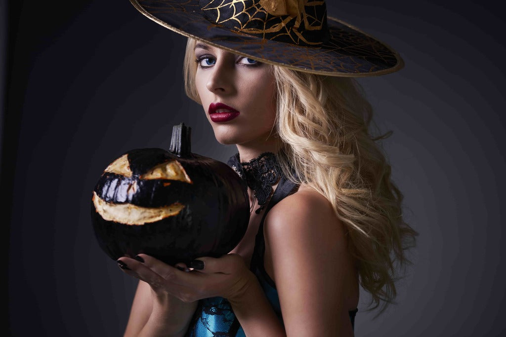 Halloween wardrobe, woman with dark witch makeup holding a pumpkin.