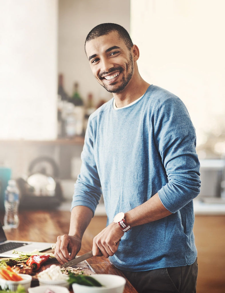 Young man smiling while cutting vegetables in preparation for a meal