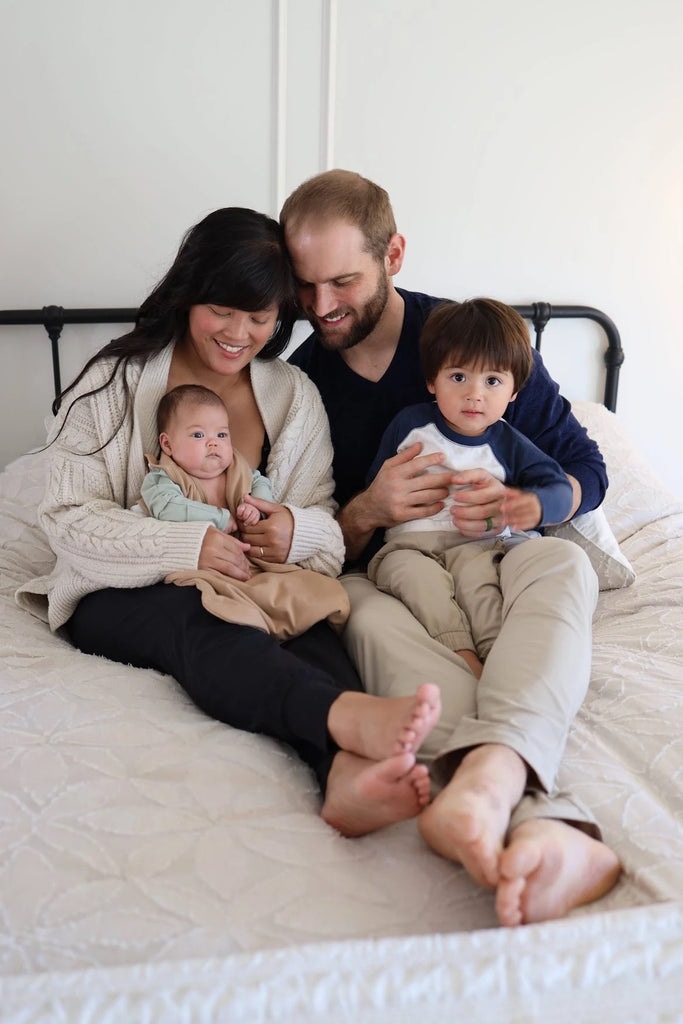 January, Drew, Mason, and Mira sitting on their bed admiring baby Mira.