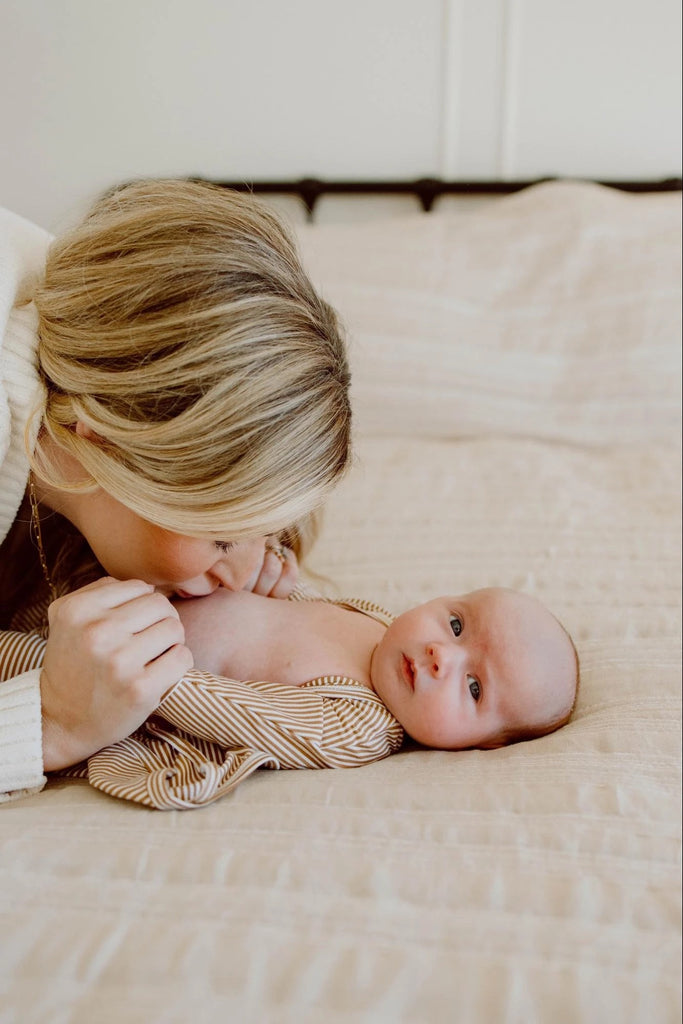 A mom kisses her baby's belly after opening the front of Bonsie's Mocha Twist Footie