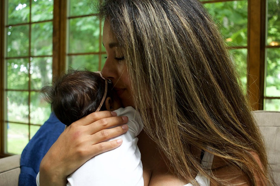 A mother holding and kissing her baby who is calmly nestled in her arms. 