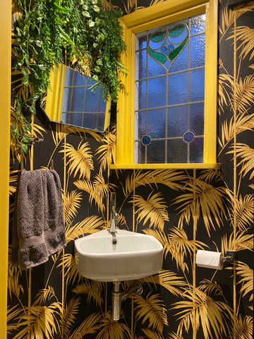 Understair bathroom using black and yellow wallpaper, yellow painted window frames and woodwork plus lots of fake plants