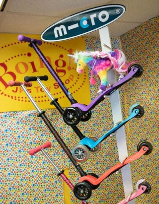 Micro scooters display with purple, blue, and red scooters and a plush unicorn riding on.