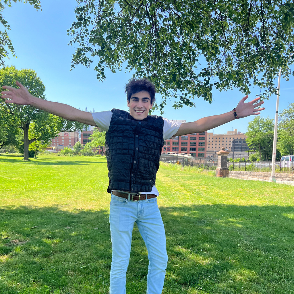 A boy with his hand raised high, wearing a black vest.