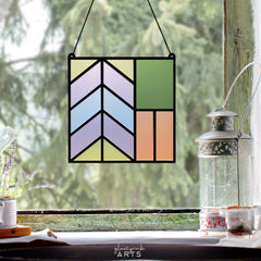 A geometric stained glass panel made from laser cut acrylic hung in a window against a forest backdrop