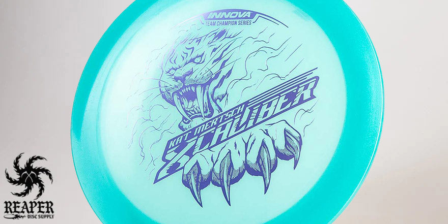 An aqua colored Innova Champion Glow XCaliber (Kat Mertsch Tour Series) disc with purple stamp