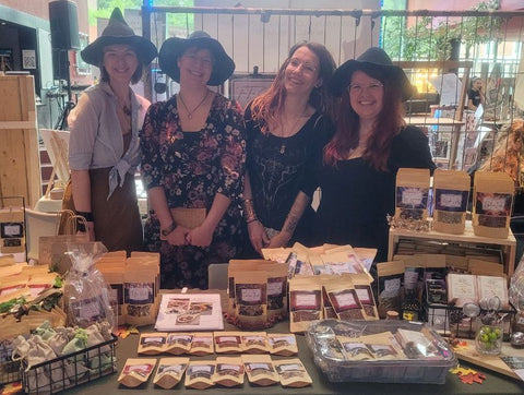 The four Tea Coven witches at a market stall with lots of tea.