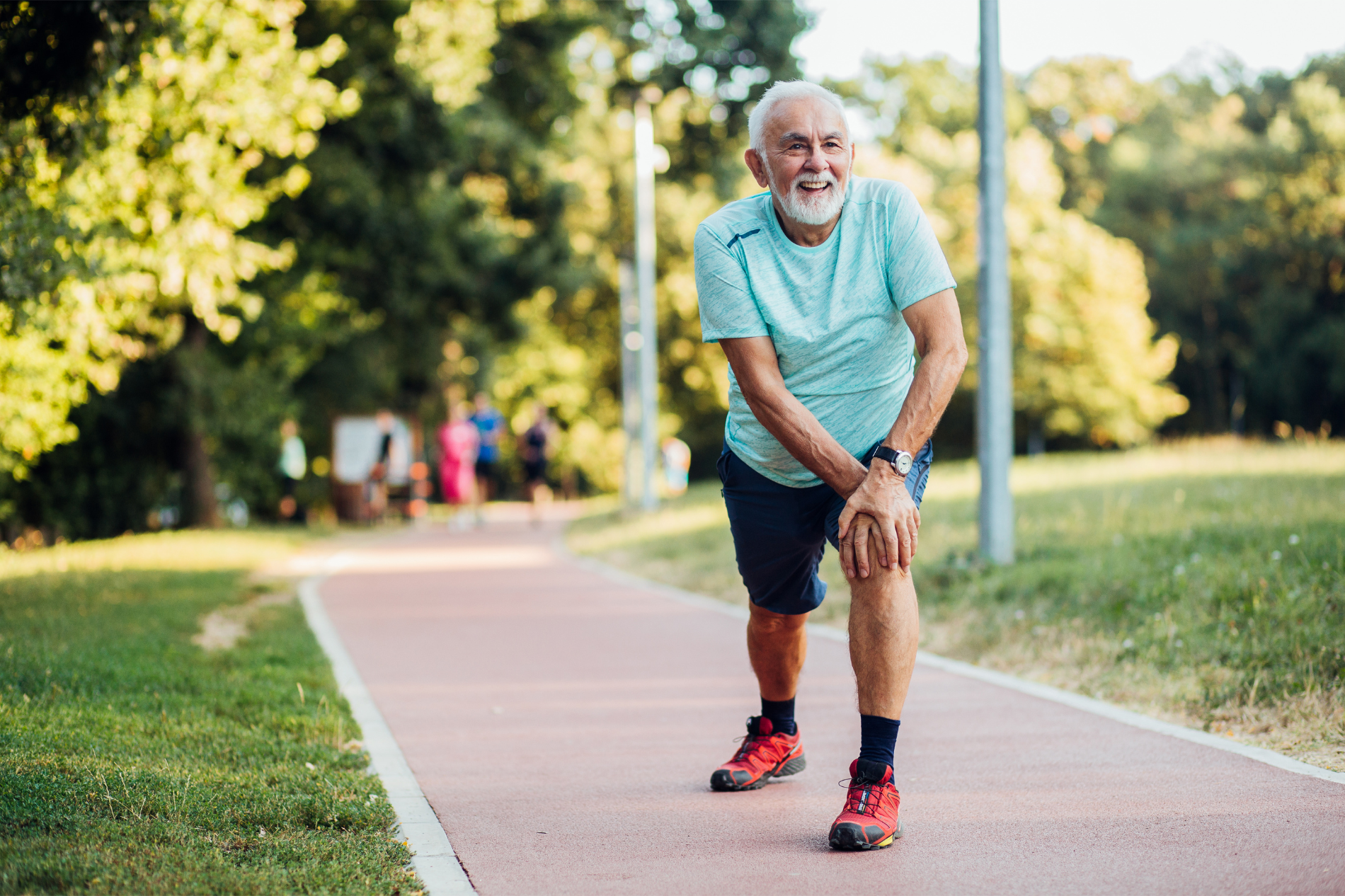 Elderly man smiling while stretching on a park path.