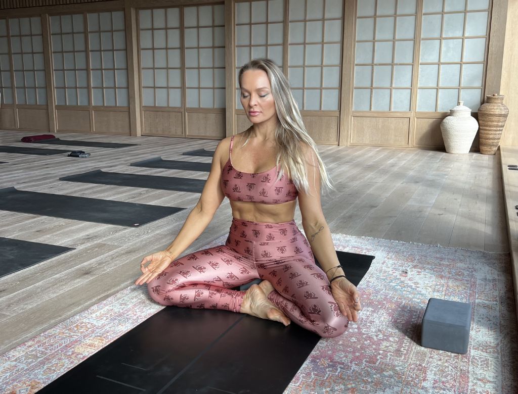 Mulher com legging e top fazendo posição de yoga no chão