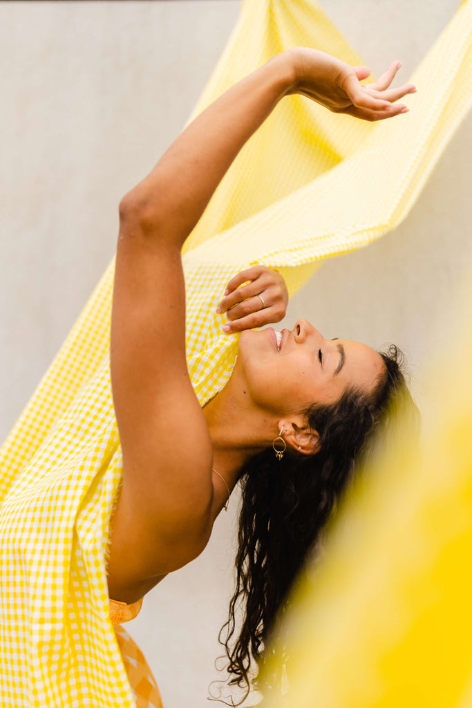 Interview with Rosie Lugg @rambosphotos. Portrait of a young girl with her eyes clothes, hands in the air. She is draped in a yellow sheet.