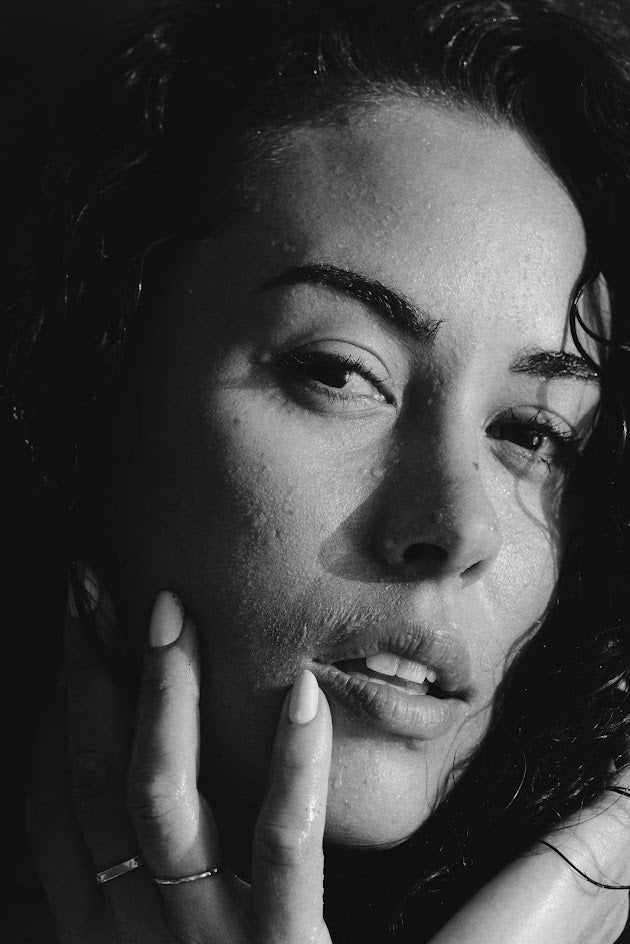 photo taken by photographer jac lee. black and white image, a moody close up of a girl with her hand lightly touching her face, half her face in shadow