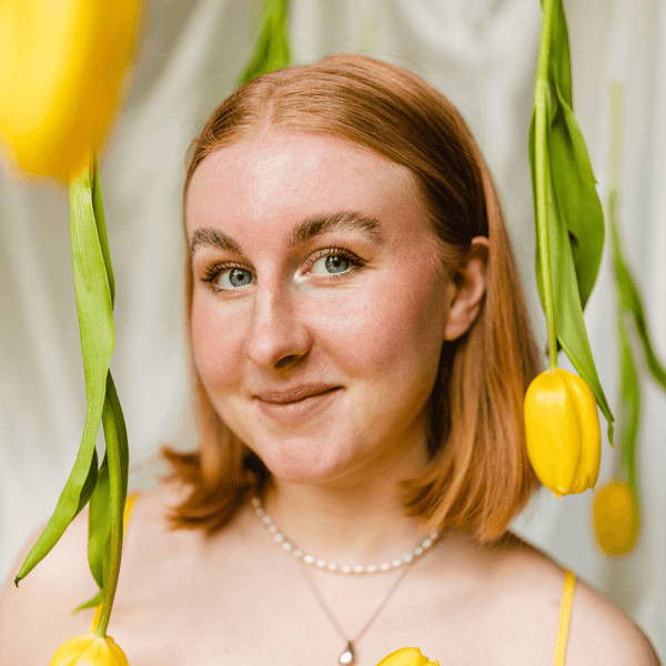 Interview with Rosie Lugg @rambosphotos. Portrait of a girl with short auburn hair, she is surrounded by yellow tulips hanging from the ceiling