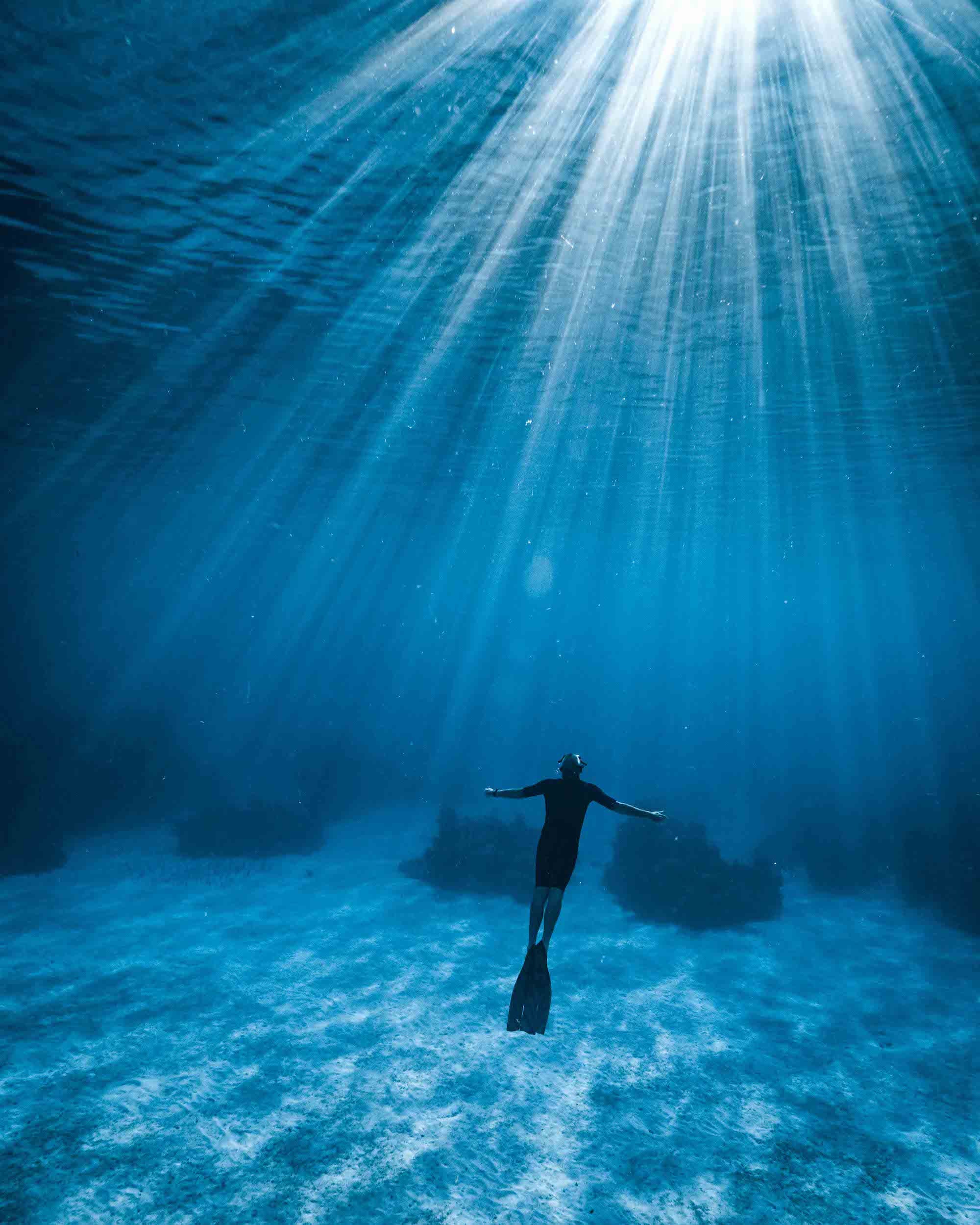 Under the water, the suns rays shine down into the depths as a lone diver swims towards the surface. Image by photographer Hannah Prewitt.