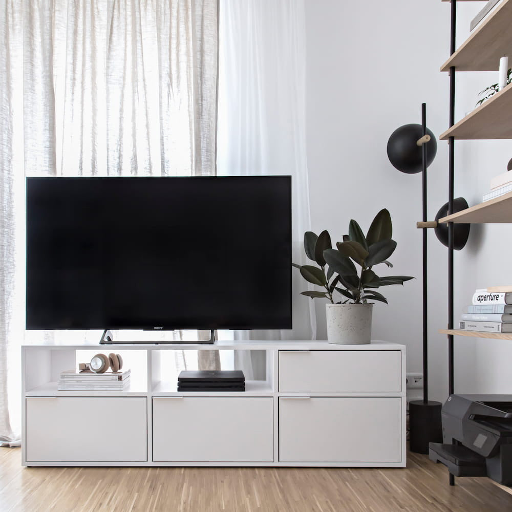 A white TV stand with a TV and potted plants on it