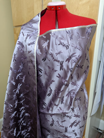 A lavender and purple brocade with a dragonfly design is draped over a dressform.