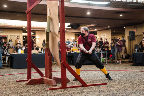 SoCal Swords instructor Myles Cupp successfully cutting tatami wrapped around wooden dowel hidden behind paper during SoCal Swordfight 2022, spectators in background