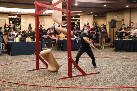 Competitor at SoCal Swordfight successfully cutting two cuts on the piece of paper while crowd watches