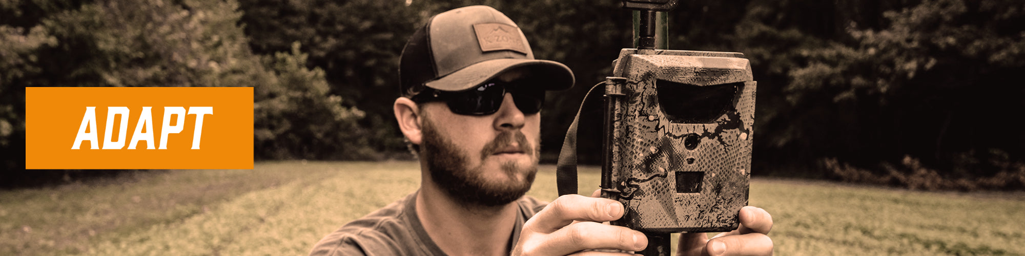 Text on image saying, "adapt". A man sets up a spartan camera on a pole. The background is blured with grass and trees.